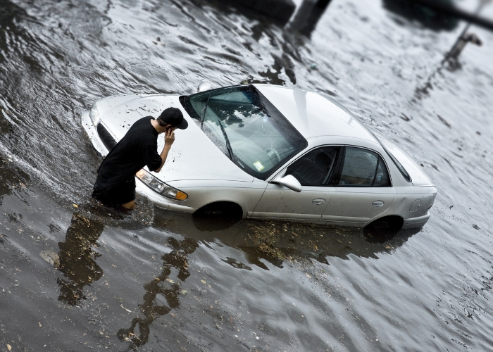 joven afuera de su auto inundado por las lluvias